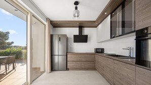 Eine moderne Küche mit integriertem Kühlschrank, Mikrowelle und Backofen, Holzschränken und einem großen Fenster mit Blick auf eine Terrasse.