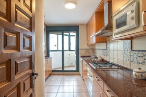 Una cocina con armarios de madera, estufa a gas, microondas y vistas a través de un ventanal.