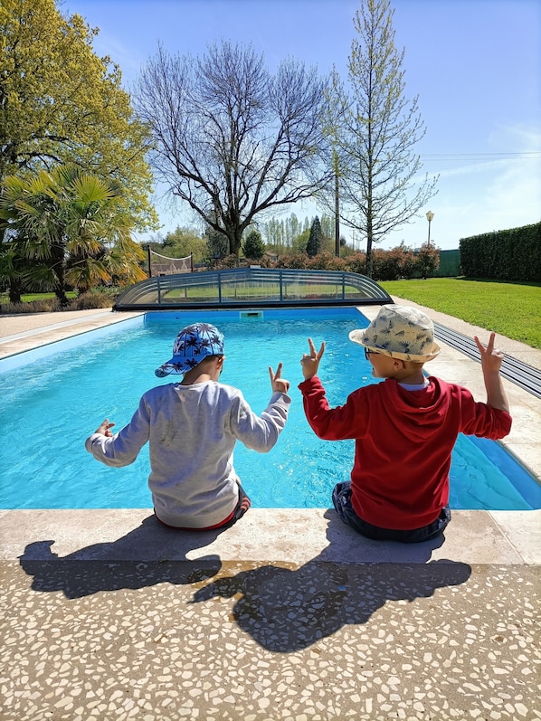 Zwei Kinder sitzen am Pool, im Hintergrund ein klarer Himmel und Bäume.