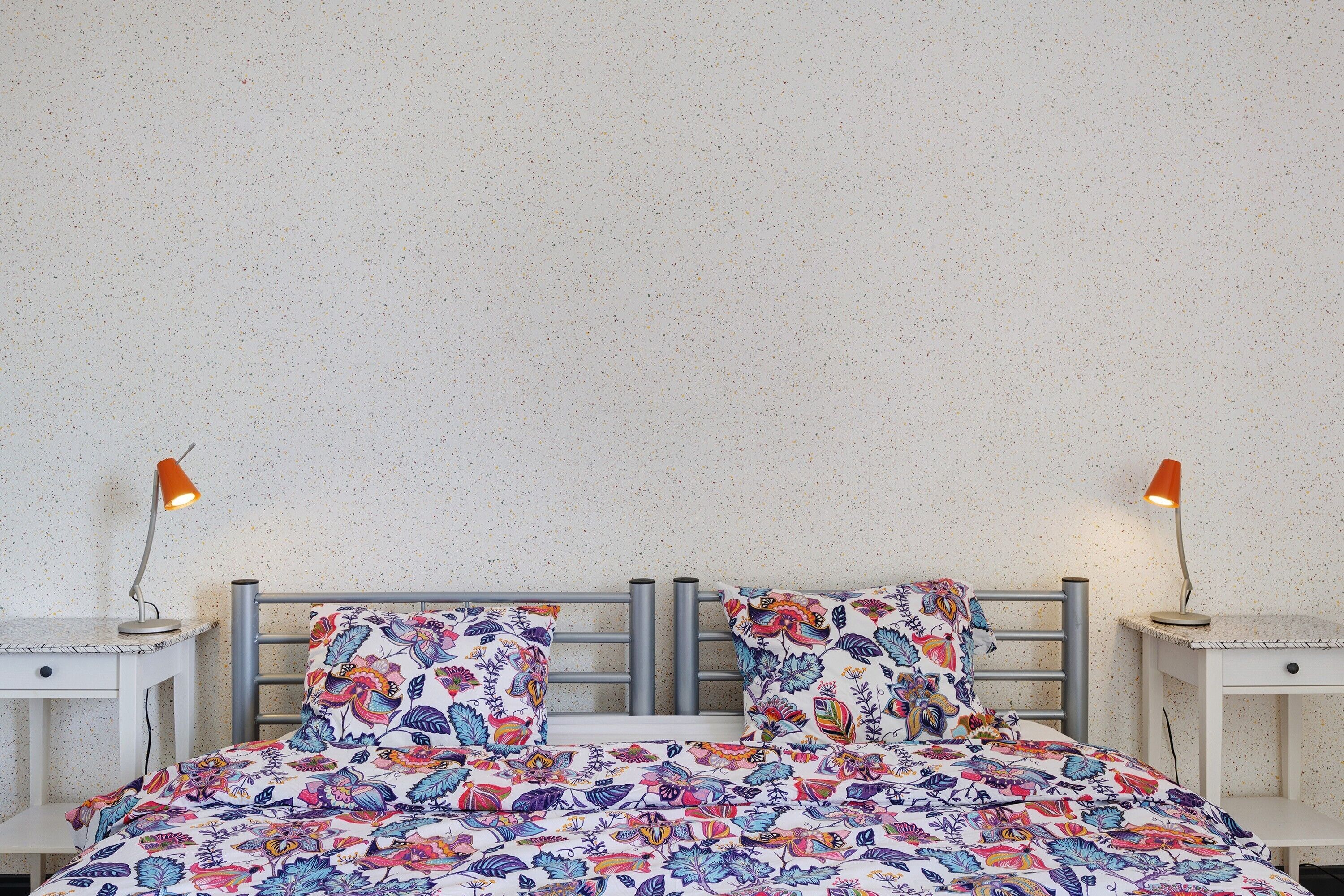 A bed with floral bedding, a metal headboard, bedside tables, and two lamps.