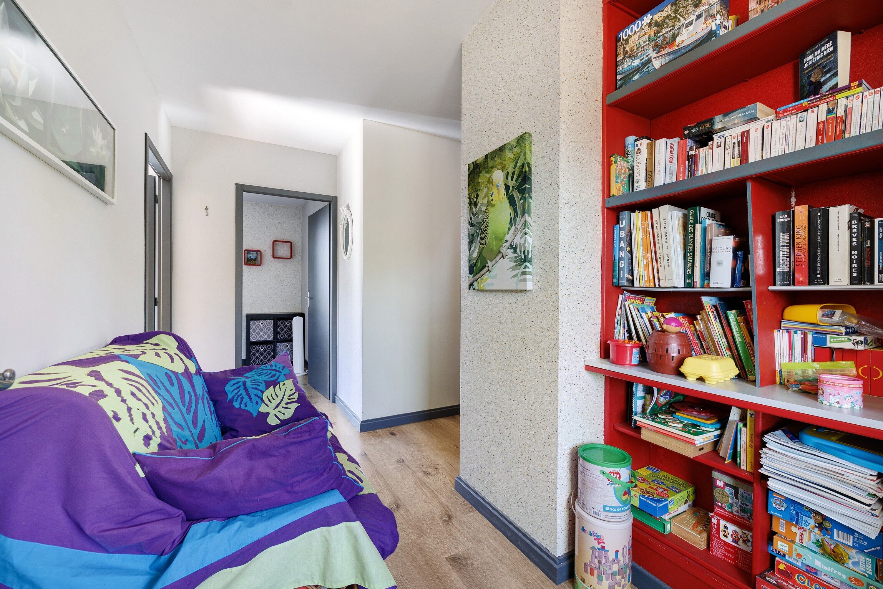 A bedroom with a bed, a bookshelf, and a door leading to another room.
