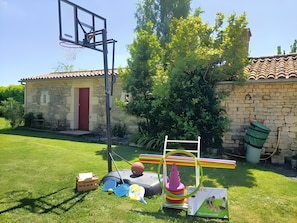 Ein Basketballkorb, eine Schaukel und ein kleines Haus mit roter Tür.