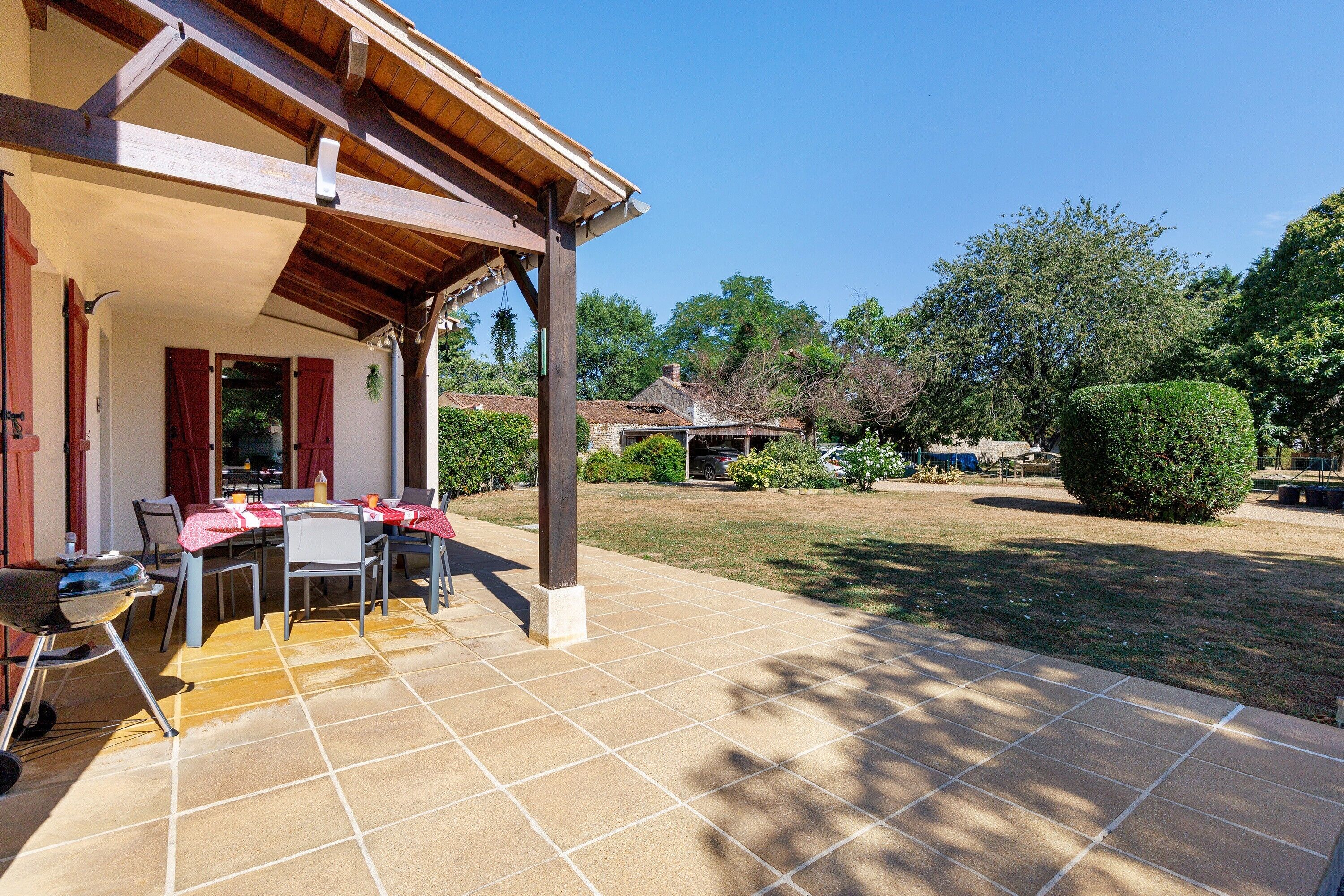 Une terrasse couverte avec une table et des chaises, un barbecue et une vue sur un quartier résidentiel avec des arbres et une maison.