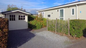 Une maison mobile avec un petit garage attenant, une allée en gravier et une clôture en bois.