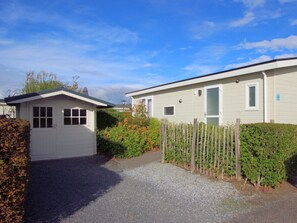 A mobile home with a small attached garage, a gravel driveway, and a wooden fence. - Holiday Home in Breskens With Terrace (Breskens)