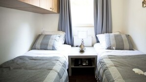 Une chambre avec deux lits, une armoire en bois, un radiateur et une fenêtre avec des rideaux.