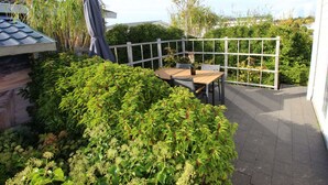 Une terrasse avec une table et des chaises, entourée de verdure et d’une clôture blanche.