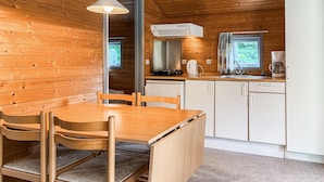 A compact kitchen with wooden walls, a dining table with chairs, a built-in stove, and a window with curtains.