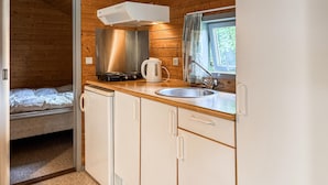 A compact kitchenette with a stove, kettle, and sink, adjacent to a bed in a cabin-style room.