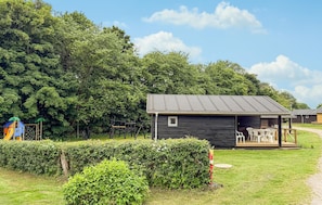 Une petite cabane dotée d’un porche et de meubles d’extérieur, entourée d’une végétation luxuriante et d’arbres.