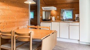 Una cocina compacta con paredes de madera, una mesa de comedor con sillas, una estufa integrada y un ventanal con cortinas.