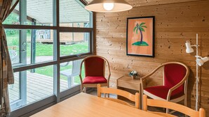 Una habitación con paneles de madera, dos sillas rojas, una mesa de madera y vistas amplias a través de ventanas grandes.