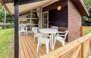 En træhytte med terrasse, hvide plastikstole og et rundt bord.