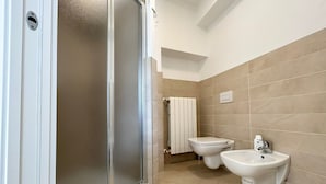A bathroom with a shower, toilet, bidet, and a towel rack.