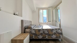 A bedroom with a bed, a nightstand, a window with a mountain view, and a radiator.