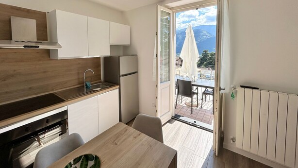 A modern kitchen with white cabinets, a stainless steel range hood, and a view of a patio with outdoor furniture.