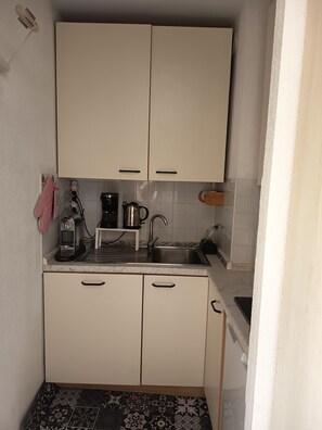 Eine kleine Küche mit zwei Schränken, einem Spülbecken, einer Kaffeemaschine und einem Wasserkocher.