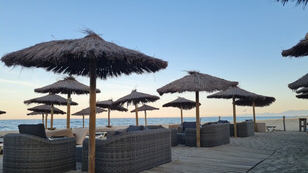 A beachside lounge area with wicker furniture and thatched umbrellas.