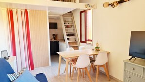 A compact living space with a dining area, a sofa, a TV, and a kitchen in the background.