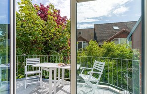 Ein Balkon mit Tisch und Stühlen, einer Glastrennwand und Blick auf ein Haus mit Ziegeldach.