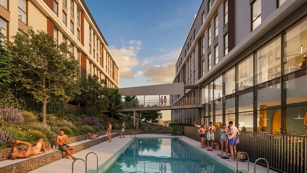 Area piscina con un edificio completamente vetrato su un lato e una passerella coperta sull'altro.