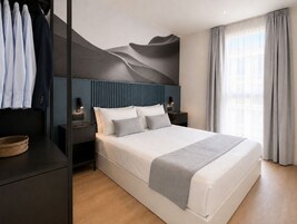 Un dormitorio moderno con una cama grande, un cabecero con líneas verticales, mesitas de noche con lámparas y vistas al exterior a través de una ventana con cortinas.