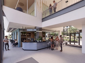 A modern interior with a central bar area, seating, and a balcony with people.