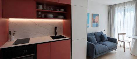 Una cocina moderna con horno empotrado, un lavabo y una encimera. En la zona de estar contigua hay un sofá azul y una mesita.