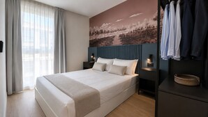 Una camera d'hotel moderna con un letto grande, un armadio, un comodino con lampada e un'opera d'arte appesa al muro.