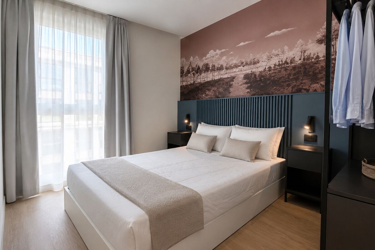 Ein modernes Hotelzimmer mit einem großen Bett, einem Kleiderschrank, einem Nachttisch mit Lampe und einem Wandbild.