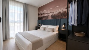 Ein modernes Hotelzimmer mit einem großen Bett, einem Kleiderschrank, einem Nachttisch mit Lampe und einem Wandbild.