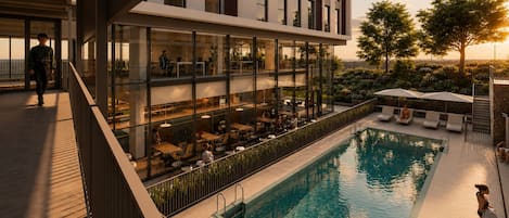 A modern building with a pool, outdoor seating, and a view of the sunset.