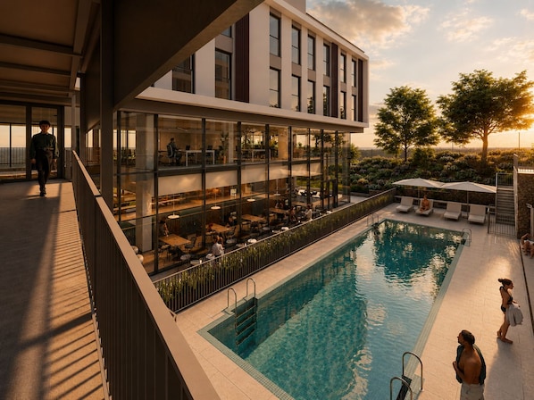 A modern building with a pool, outdoor seating, and a view of the sunset.