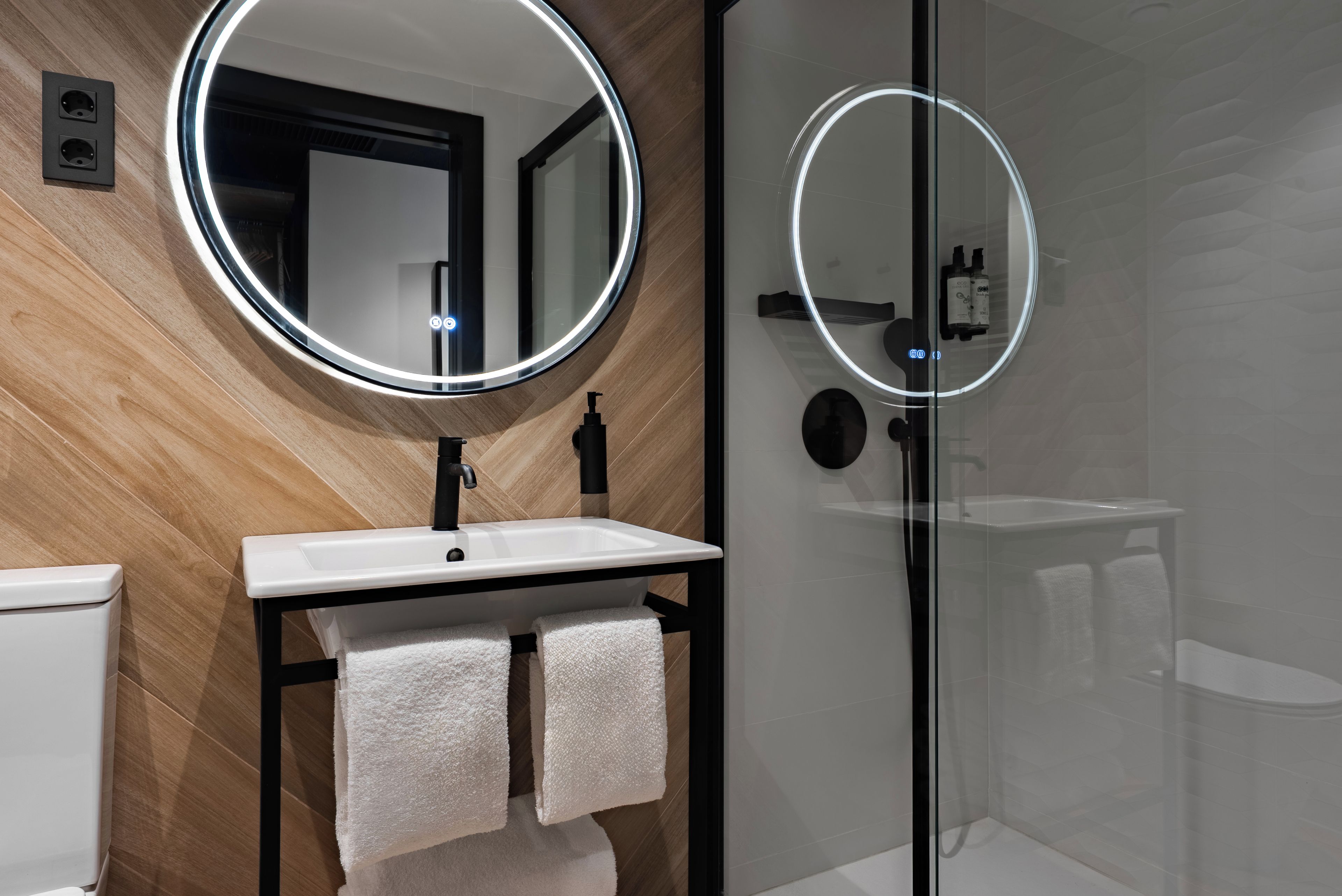 A modern bathroom with a round mirror, white sink, and glass shower enclosure.