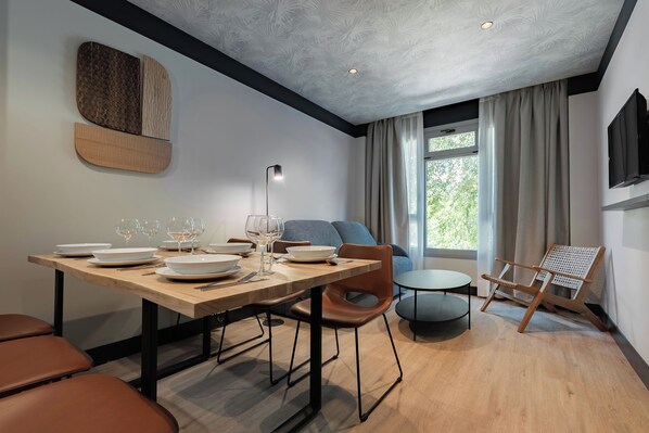 A modern dining area with a wooden table set for a meal, a sofa, a small round table, and a rattan chair.