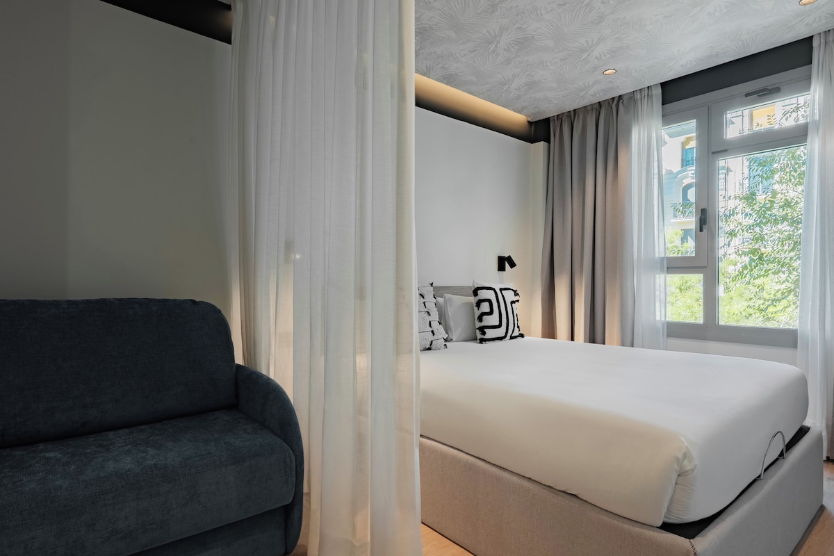 A modern bedroom with a bed, a grey sofa, and a window with curtains.