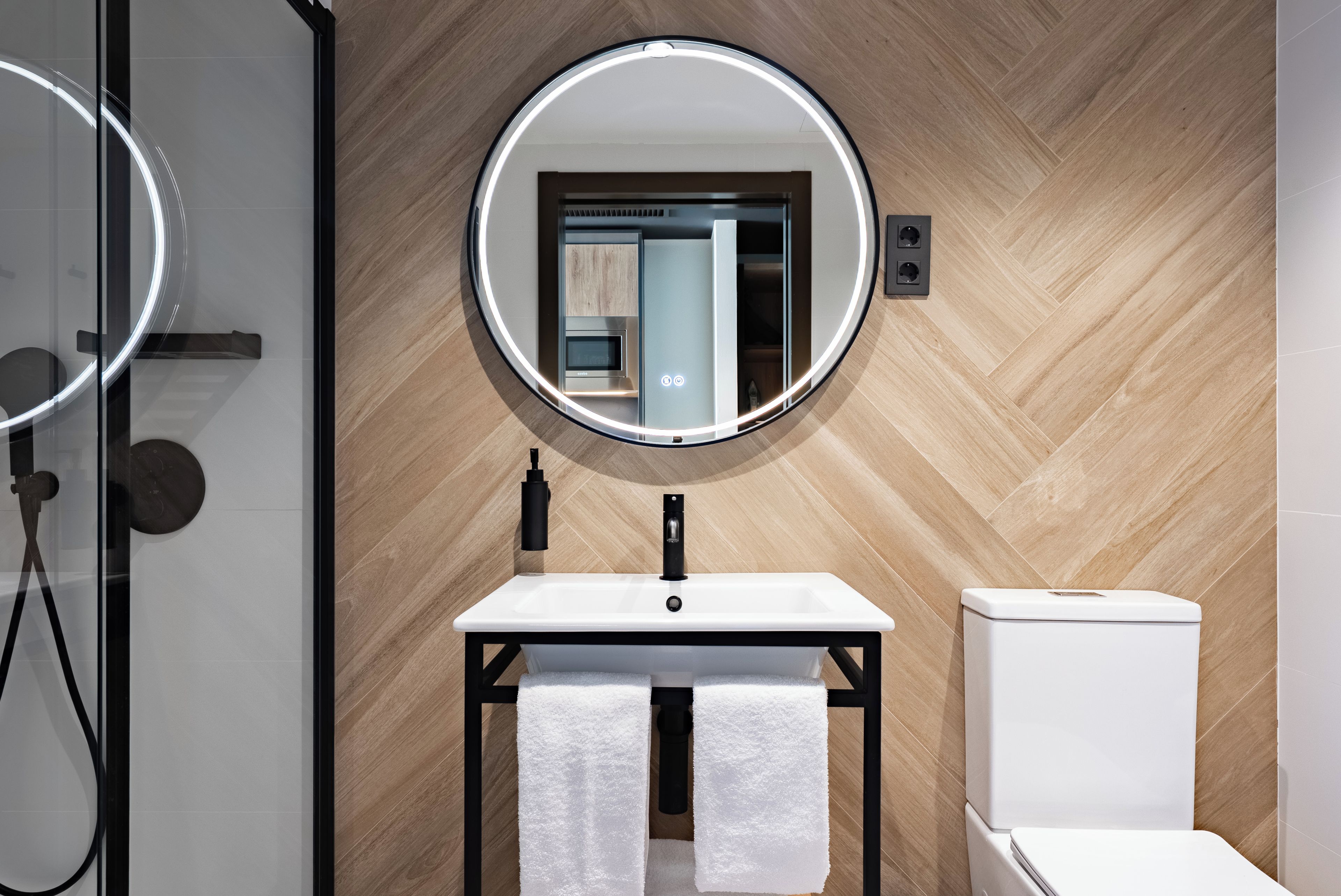 Un bagno moderno con parete in legno, uno specchio rotondo, un lavabo, un water e un porta asciugamani.