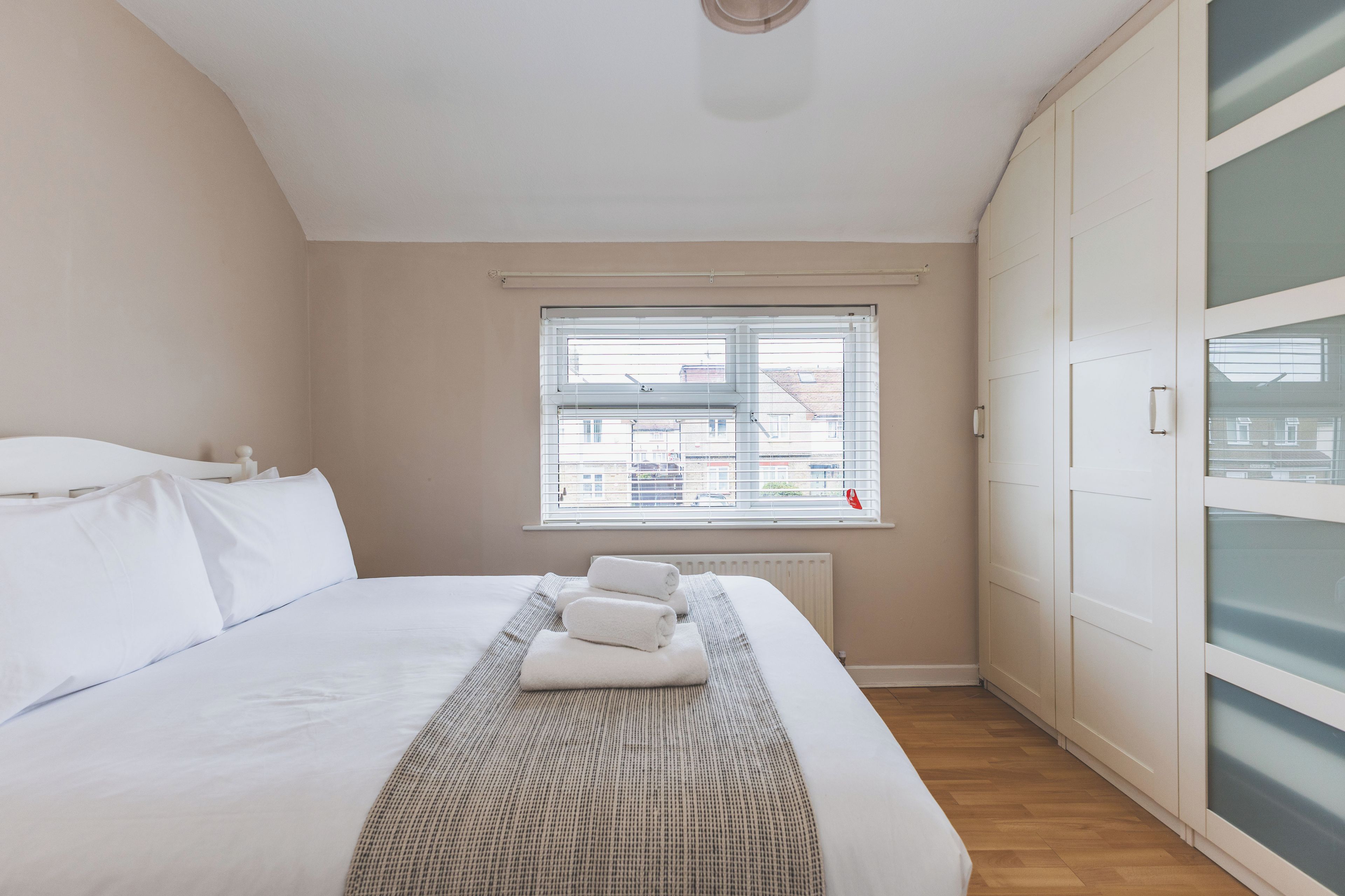 A bedroom with a large bed, a window, and a wardrobe.