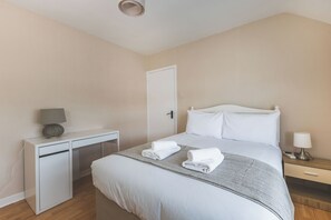 A hotel room with a bed, bedside table, desk, and a door. - Spacious 3BDR Home with Parking (Greater London)