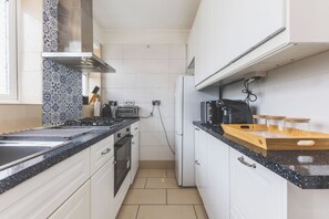 A compact kitchen with white cabinets, a black countertop, and a stainless steel range hood. - Spacious 3BDR Home with Parking (Greater London)