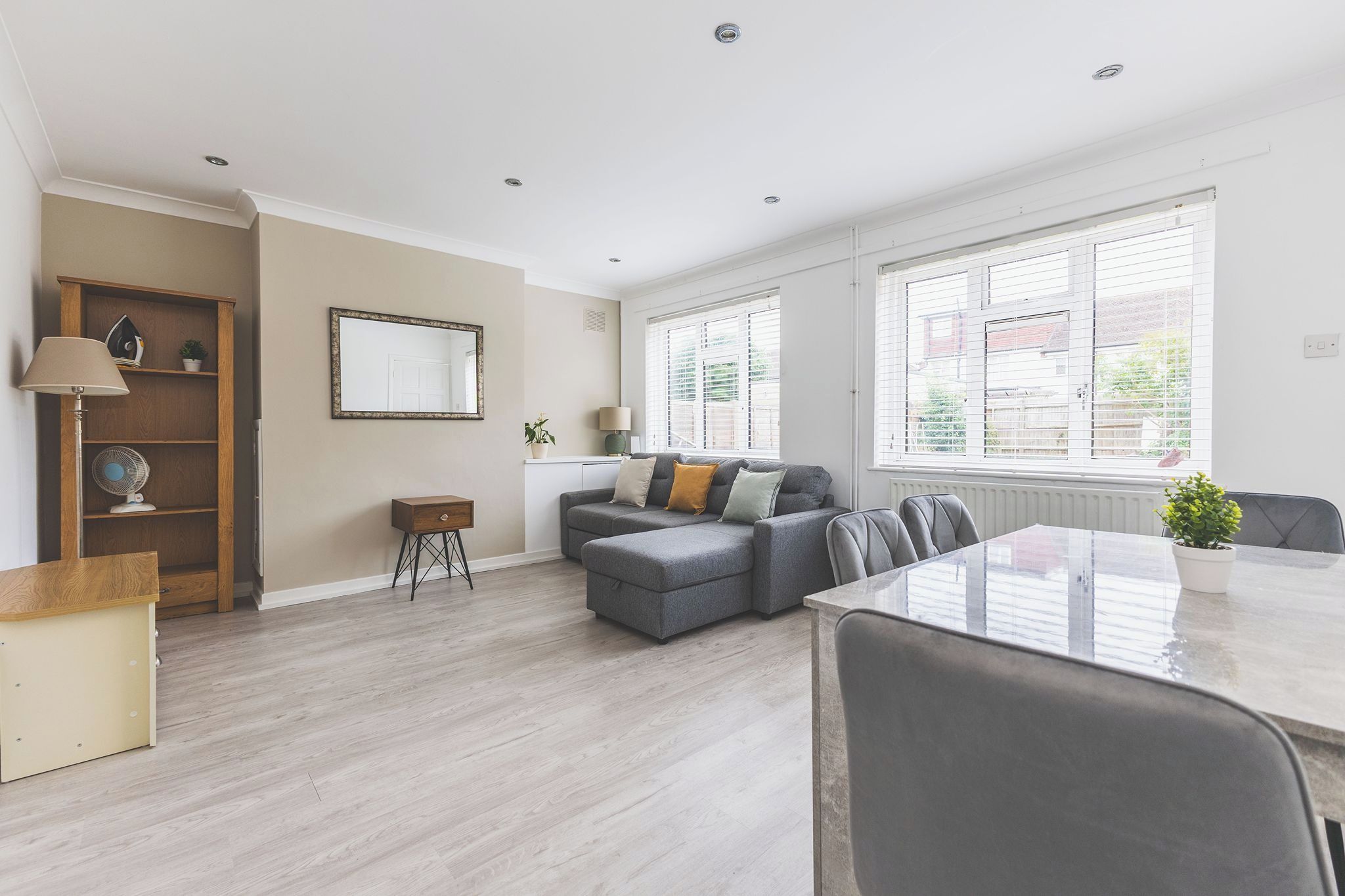 A modern living room with a grey sofa, a dining table with chairs, a small wooden cabinet, and a floor lamp.