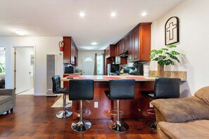 A kitchen with wooden cabinets, a central island with bar stools, a microwave, and a plant. - Long Beach 2BR - Near Beach, Driveway Parking (Long Beach)