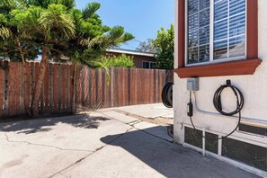 Une terrasse en béton avec une clôture en bois, un palmier et un bâtiment doté d’une fenêtre et d’un appareil de climatisation.