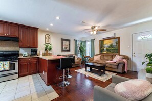Une cuisine moderne avec un îlot central, un coin repas comprenant un canapé et une table basse, et un salon avec un divan et un tableau.