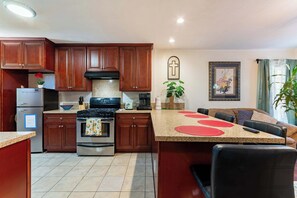 A kitchen with wooden cabinets, a stove, a refrigerator, and a dining area with a table and chairs. - Long Beach 2BR - Near Beach, Driveway Parking (Long Beach)