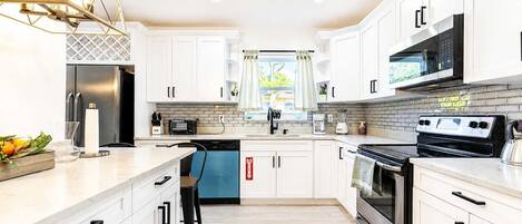Una cocina moderna con armarios blancos, un refrigerador de acero inoxidable, un microondas, una estufa y un lavavajillas.