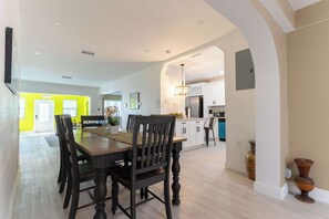 A dining area with a wooden table and chairs, a kitchen in the background, and a bright yellow room. - Hollywood 3BR - Private Pool & Fire Pit (Hollywood)