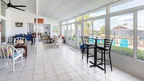 Una camera spaziosa con un'ampia finestra, un ventilatore a soffitto e un'area pranzo con sedie e tavoli.