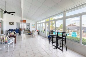 Une pièce spacieuse dotée d’une grande fenêtre, d’un ventilateur de plafond et d’un coin repas avec des chaises et des tables.
