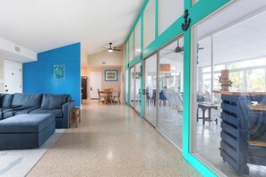 Un intérieur moderne avec un mur d’accent bleu, un canapé, un coin repas et une vue sur l’extérieur à travers une porte vitrée.